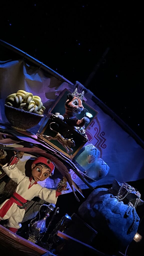 アラジンのジーニーが登場する3Dマジックショーの風景。バナナと装飾品が置かれた船内で、キャラクターの人形が描かれている。